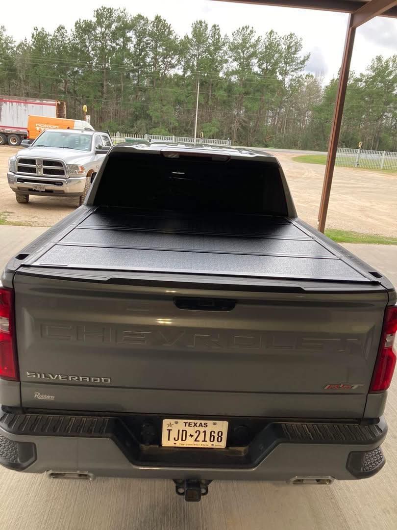 Gray pickup truck with a covered bed parked under a carport, rear view