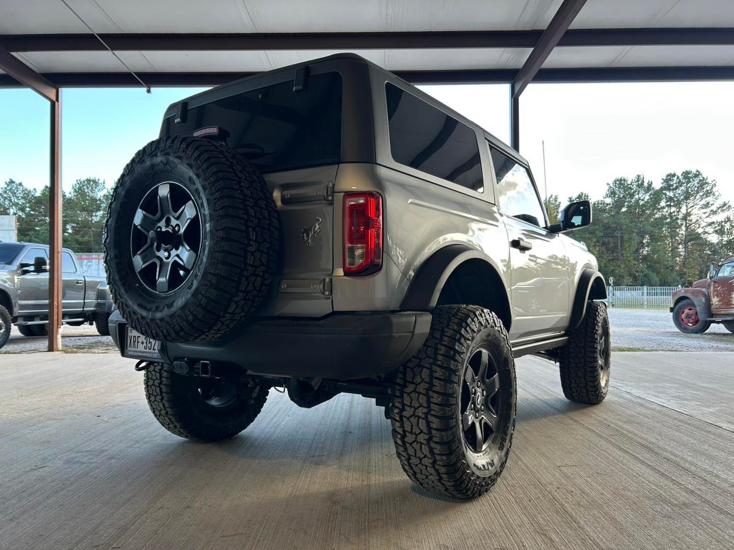 Lifted tan SUV with off-road tires and spare tire, parked under a covered structure.