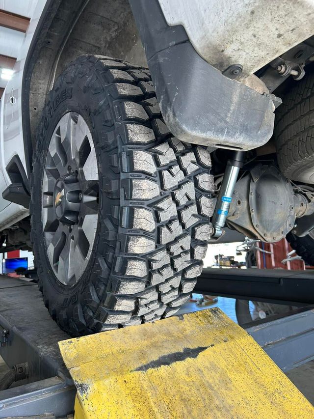 Off-road tire on a lifted vehicle on a yellow car lift ramp in a garage