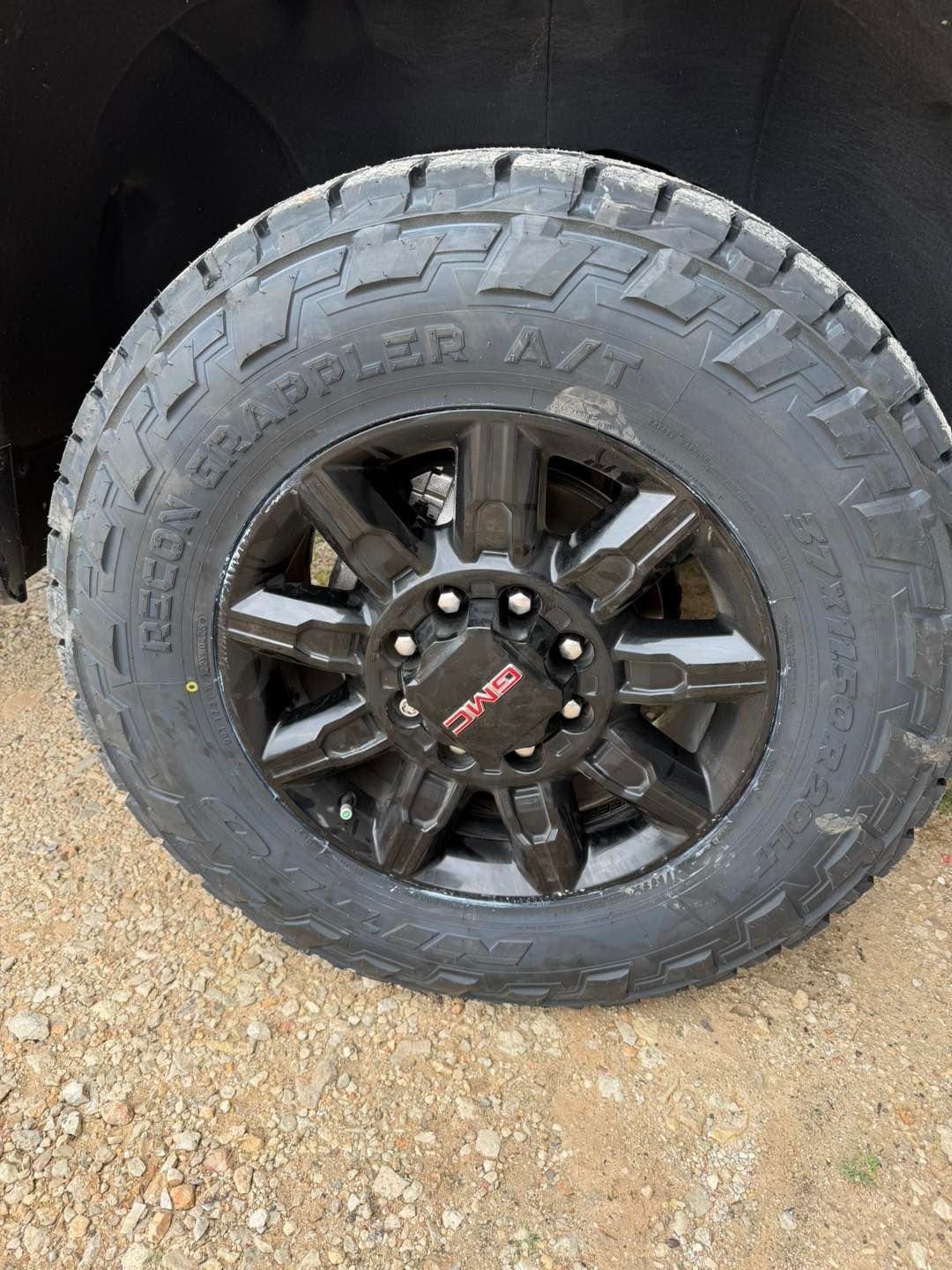 Black off-road truck wheel with rugged tire on gravel.