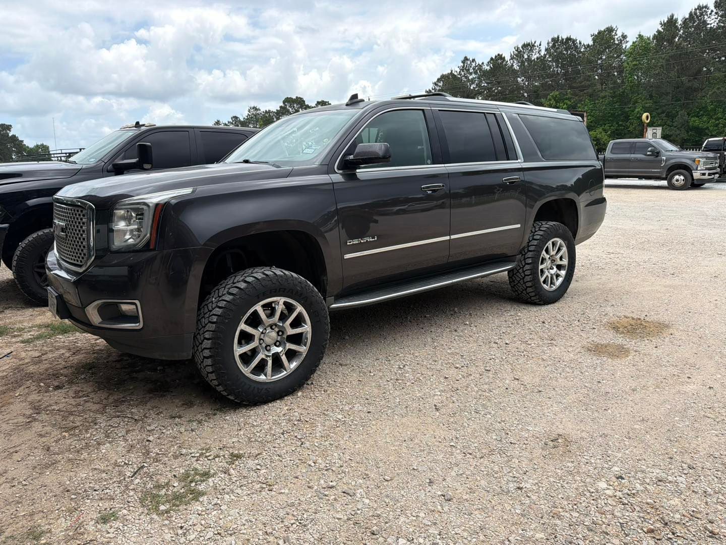 Black SUV parked on a gravel lot with trees and other vehicles in the background