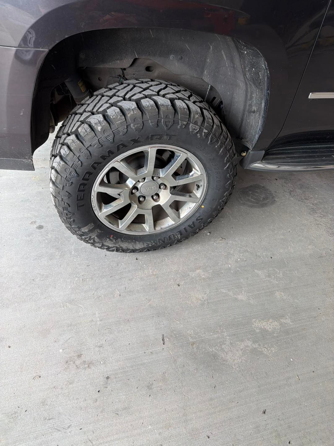 Front wheel of a black truck with an off-road tire parked on a concrete floor