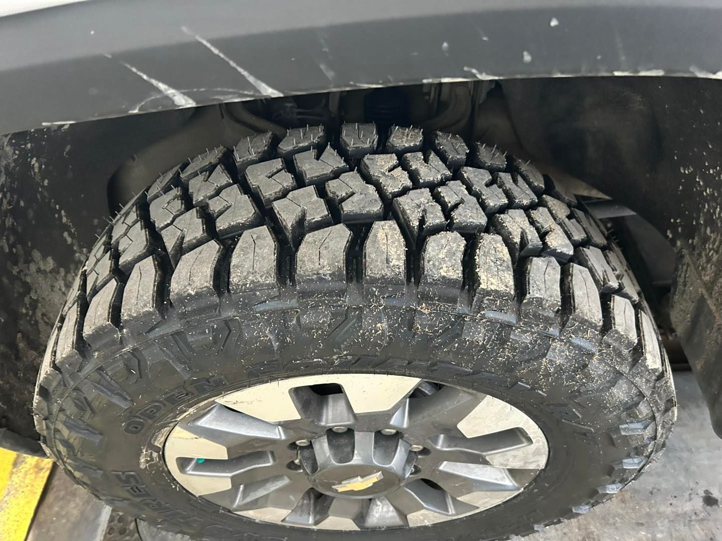 Close-up of an off-road tire with deep tread on a vehicle undercarriage, partially covered in mud.