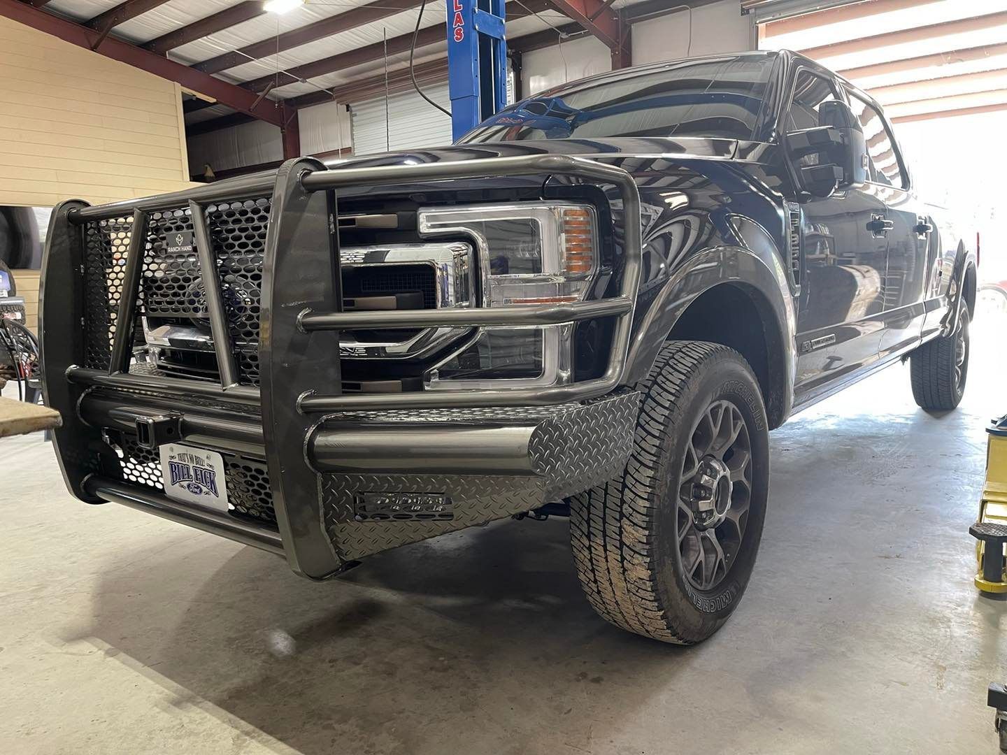Black pickup truck with bull bar and mud tires parked inside a garage or workshop.