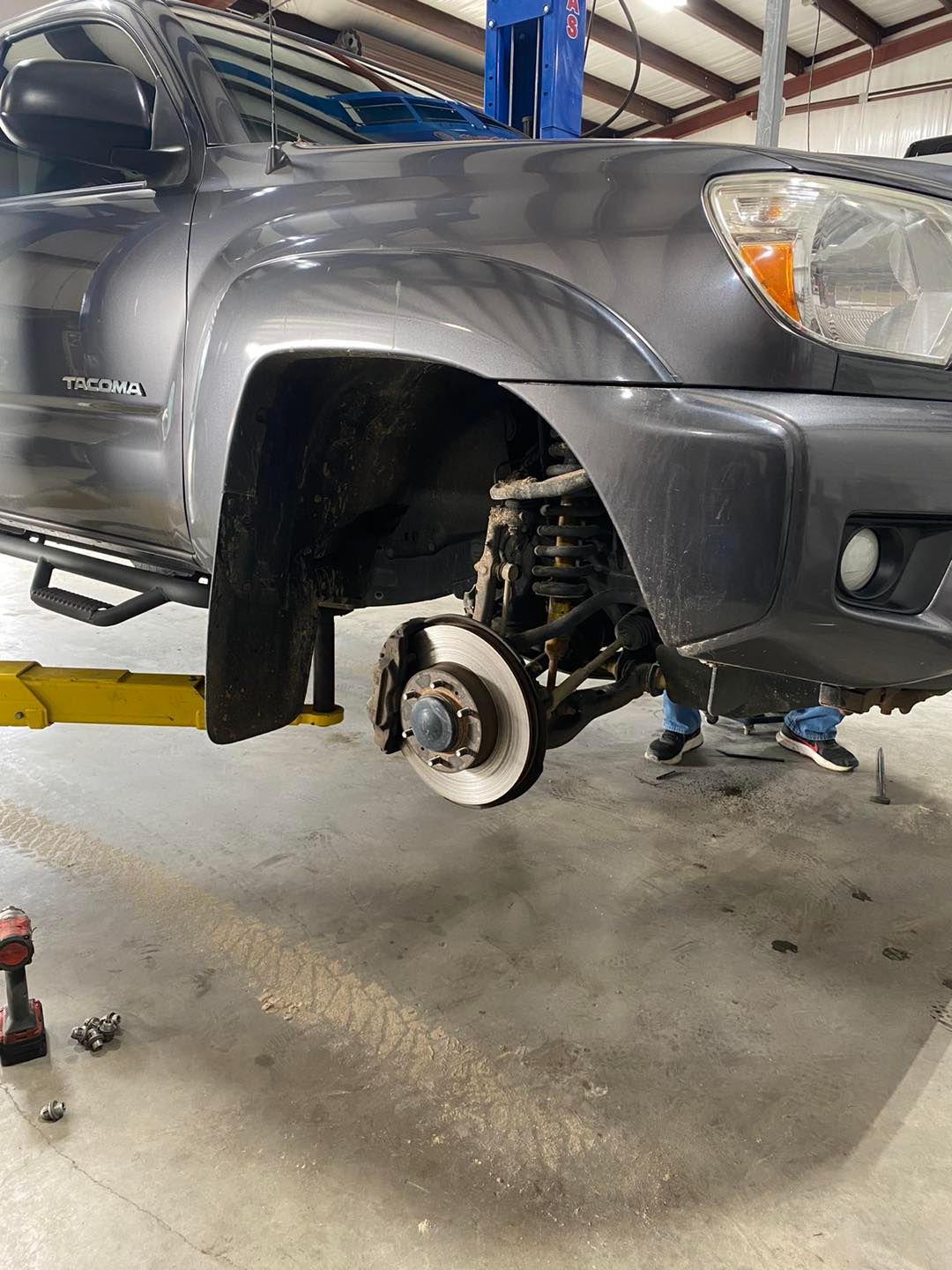 Gray SUV on a lift with the front wheel removed, exposing the brake rotor and suspension in a garage.