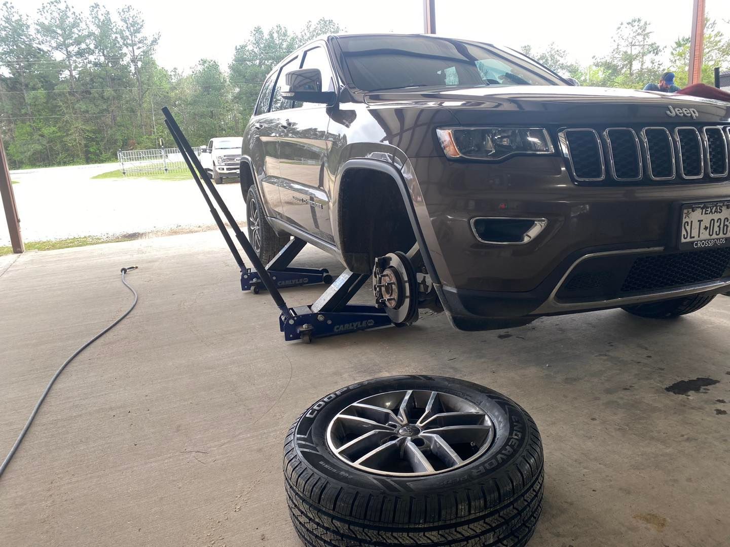 SUV raised on a jack with a detached front wheel in a driveway; tire lying in foreground.