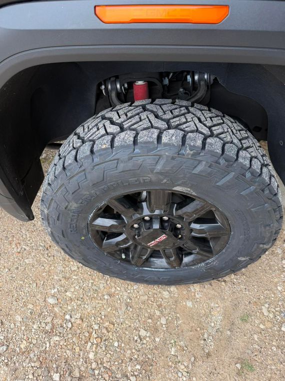 Close-up of a truck’s off-road tire and black wheel under the fender, with an orange side marker above.