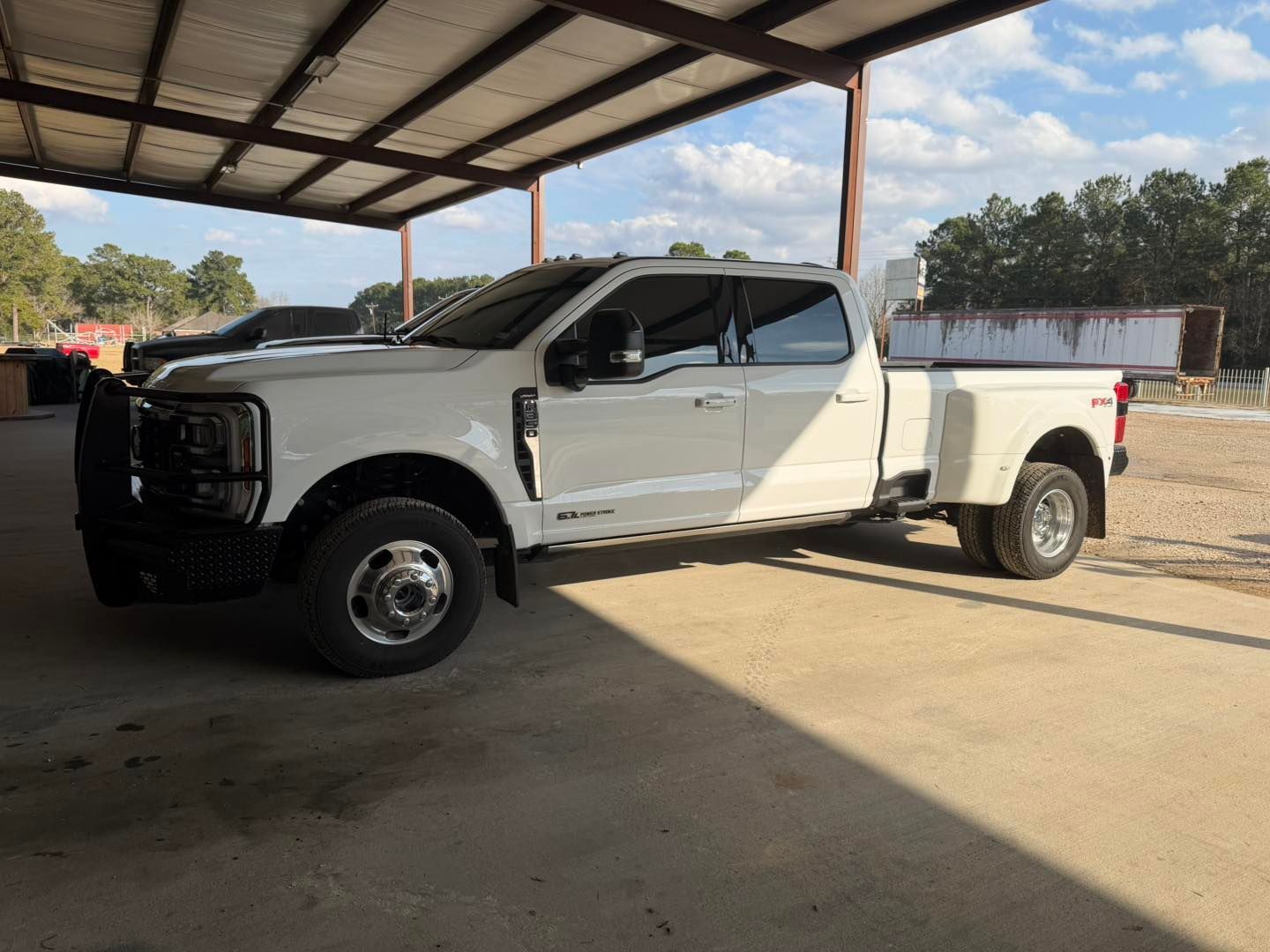 White pickup truck with open front door parked under a metal-roofed shelter outdoors