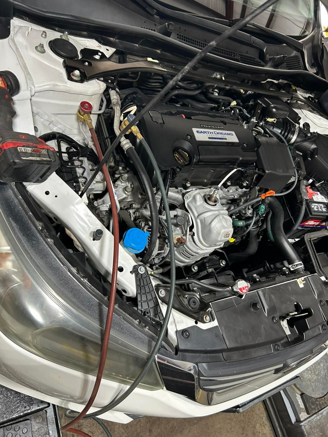 Car engine bay with exposed components and loose wiring inside a white vehicle.