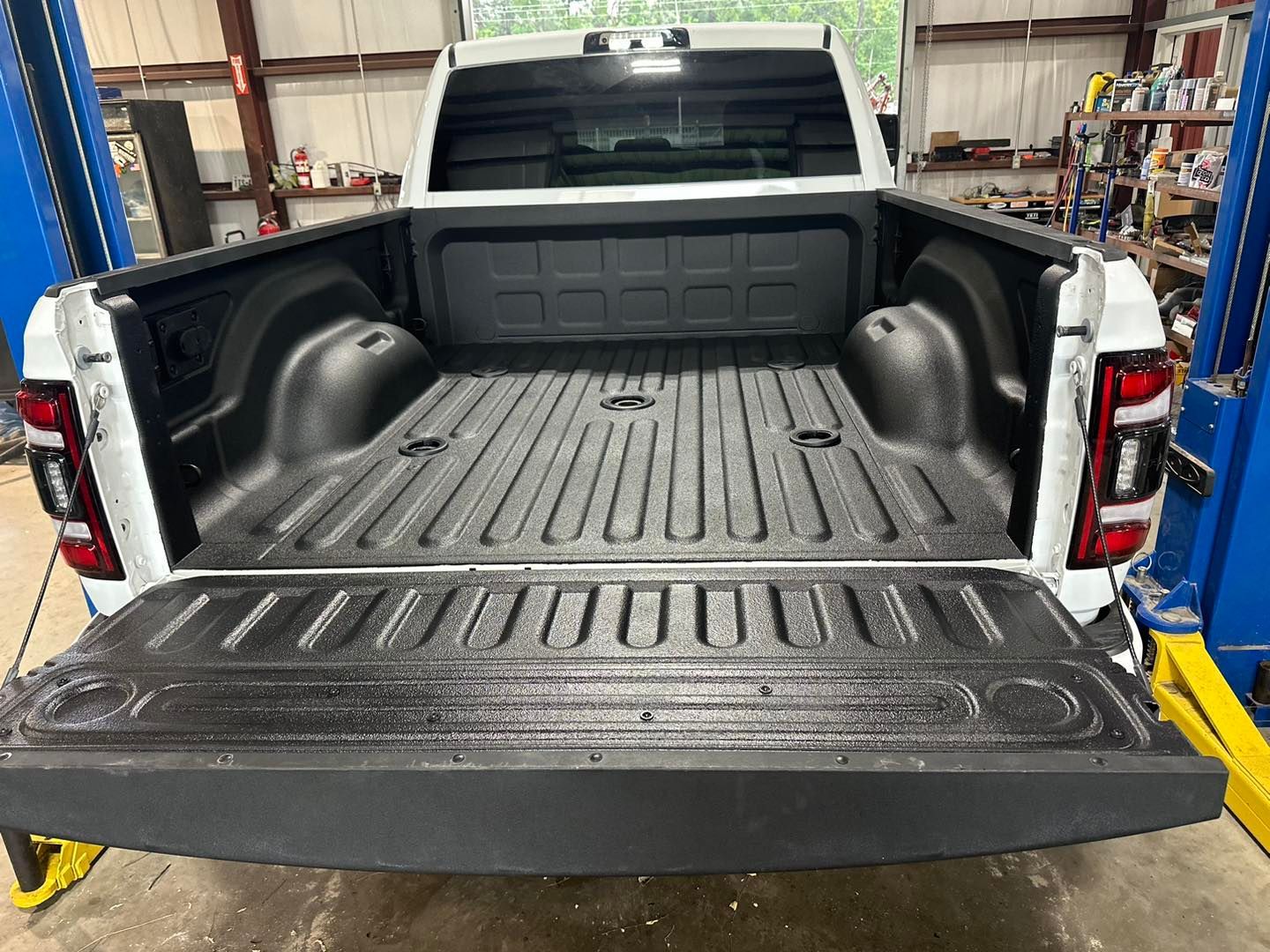 Empty black pickup truck bed with tailgate down inside a garage or workshop