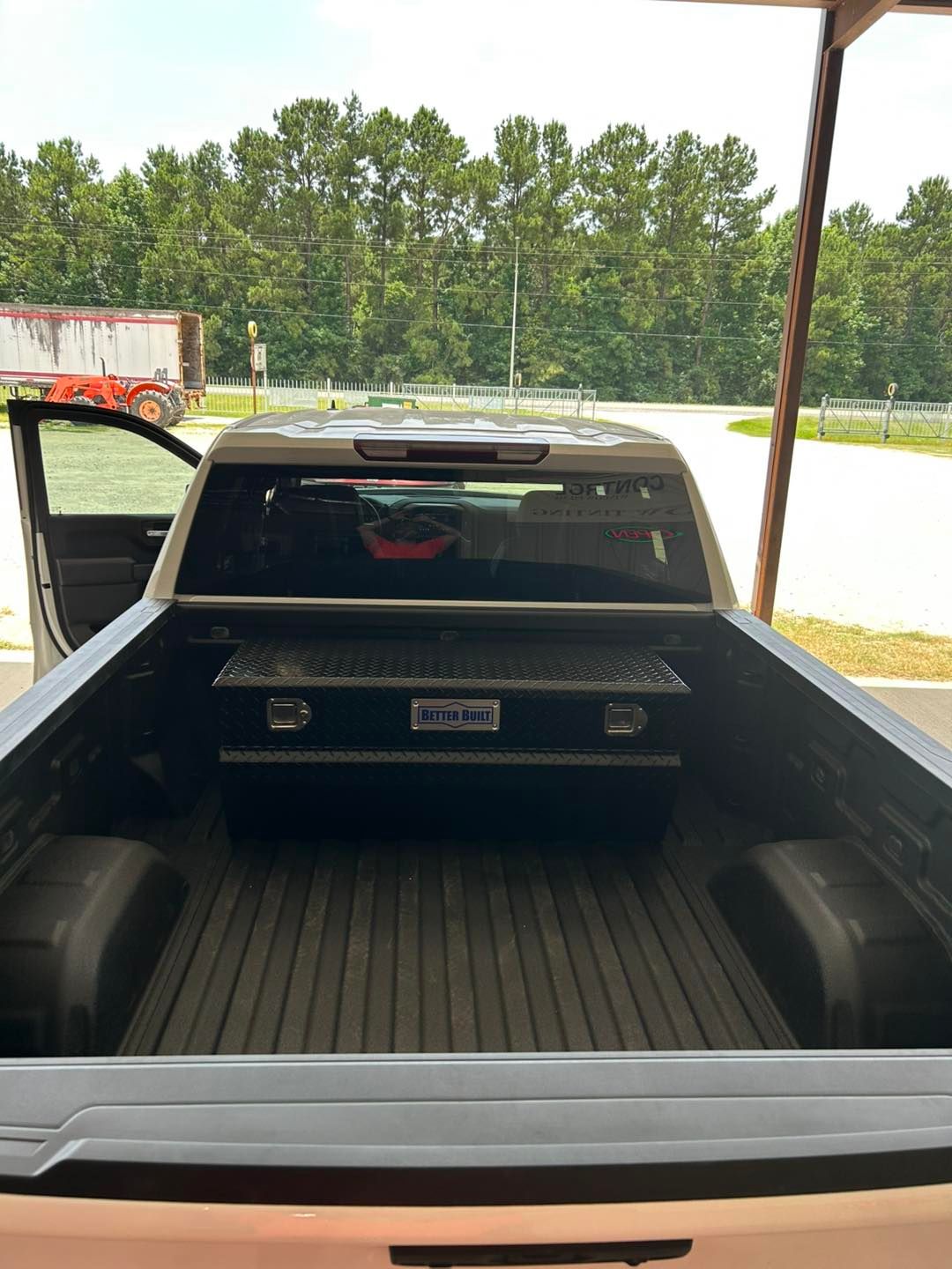 Open pickup truck bed under a carport, with the driver door open and trees in the background