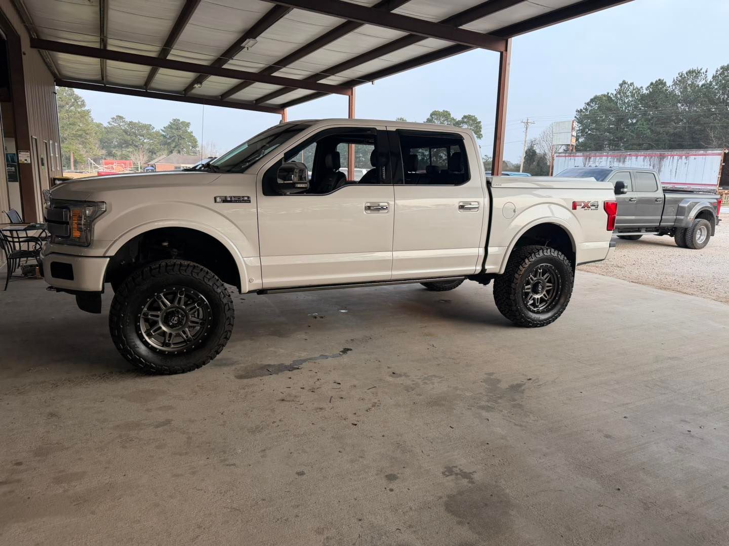 White pickup truck parked under a metal-roofed shed, side view.