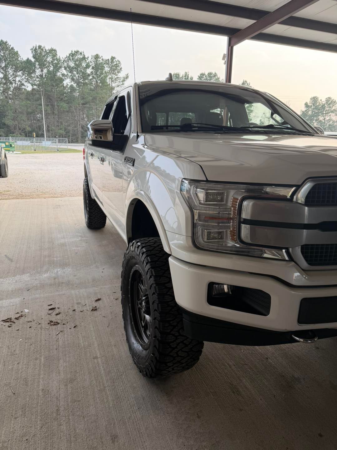 White lifted Ford pickup truck parked under a covered area on a concrete floor.