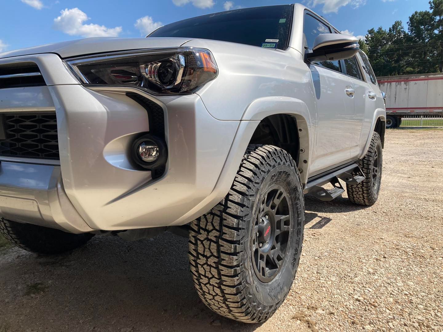 White off-road SUV with large tires parked on a gravel lot in sunlight