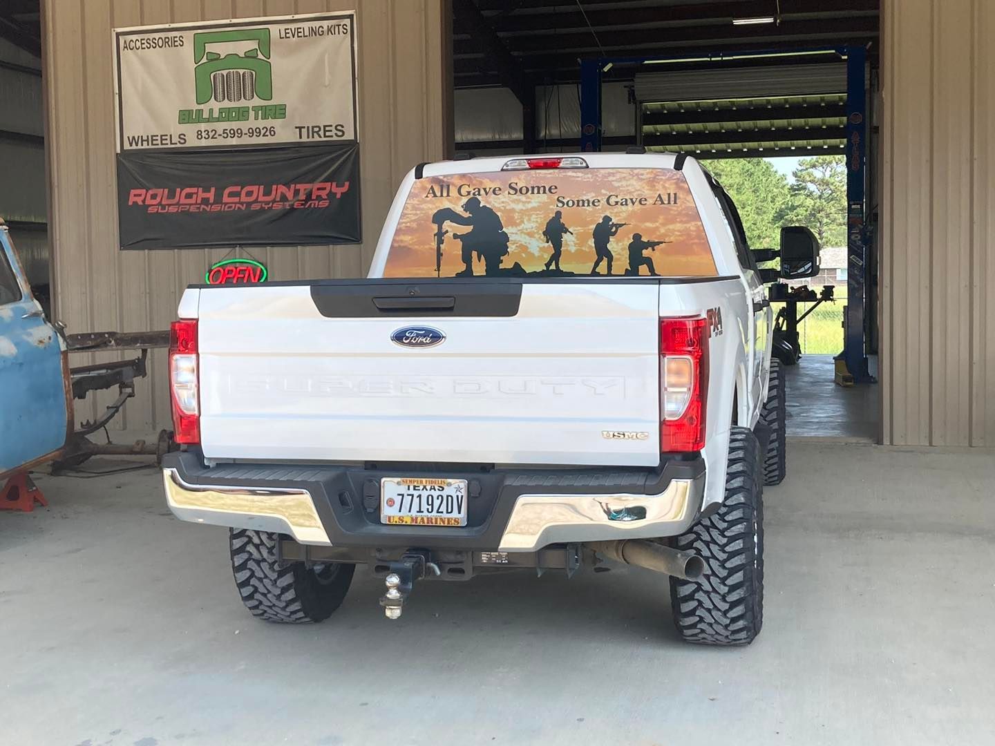 White pickup truck parked inside a garage with a mural on the rear window.