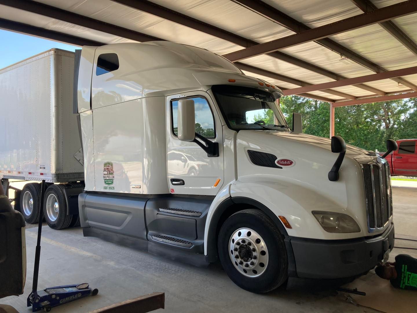 White semi-truck with trailer parked under a metal-roofed shelter.