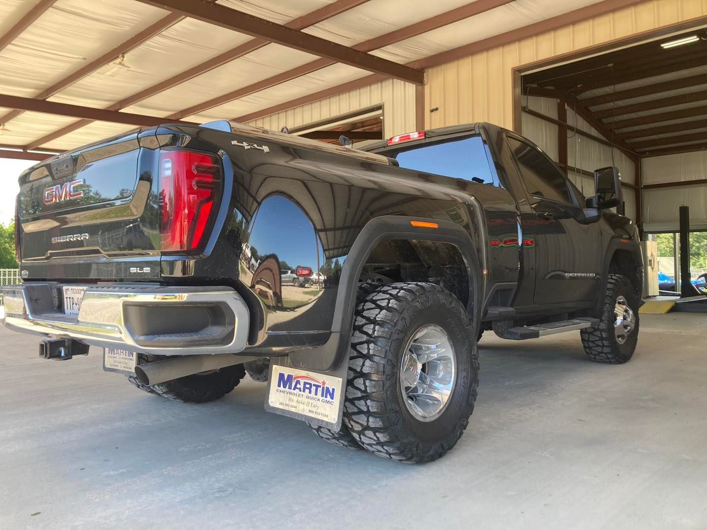 Black GMC pickup truck with lifted suspension parked inside a metal garage bay.