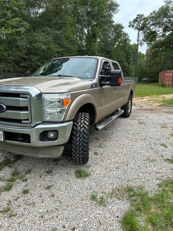 Silver Ford pickup parked on a gravel driveway beside trees and a brick wall.