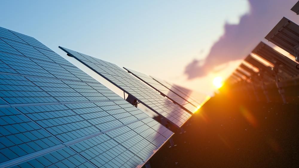 A Row Of Solar Panels Are Sitting In Front Of A Building At Sunset — Mission Solar And Electrical In Mission Beach, QLD