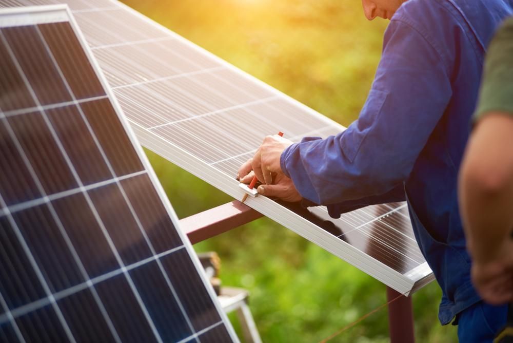 A Man Is Working On A Solar Panel In A Field — Mission Solar And Electrical In Innisfail, QLD