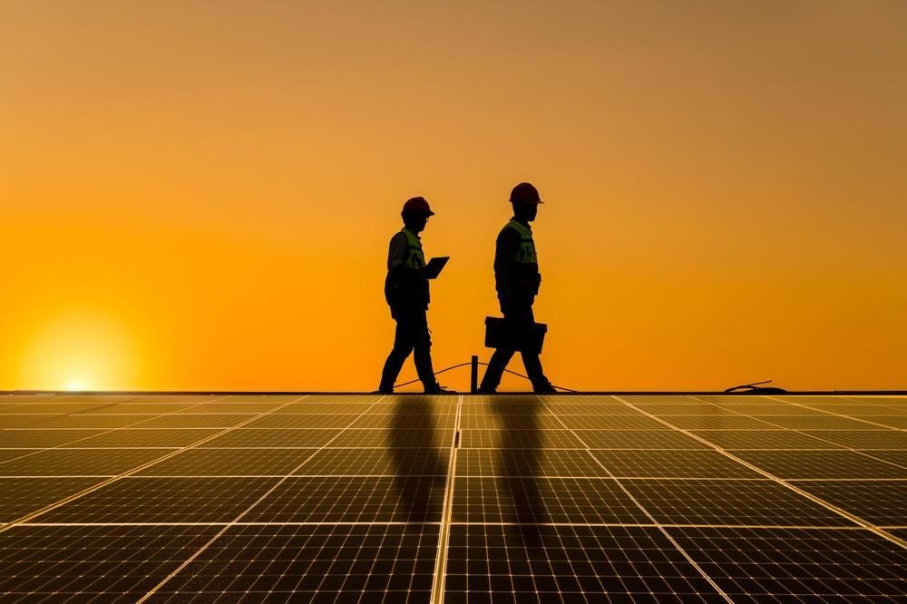 Two Men Are Walking On A Solar Panel At Sunset — Mission Solar And Electrical In Innisfail, QLD