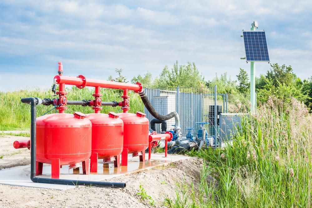 A Row Of Red Tanks Sitting On Top Of A Dirt Field Next To A Solar Panel — Mission Solar And Electrical In Tully, QLD