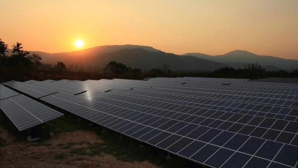 A Field Of Solar Panels With Mountains In The Background At Sunset — Mission Solar And Electrical In Tully, QLD