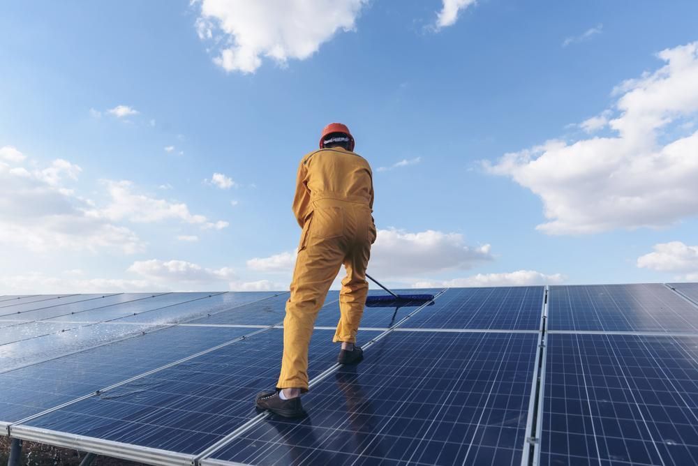 A Man Is Cleaning Solar Panels With A Brush — Mission Solar And Electrical In Cardwell, QLD