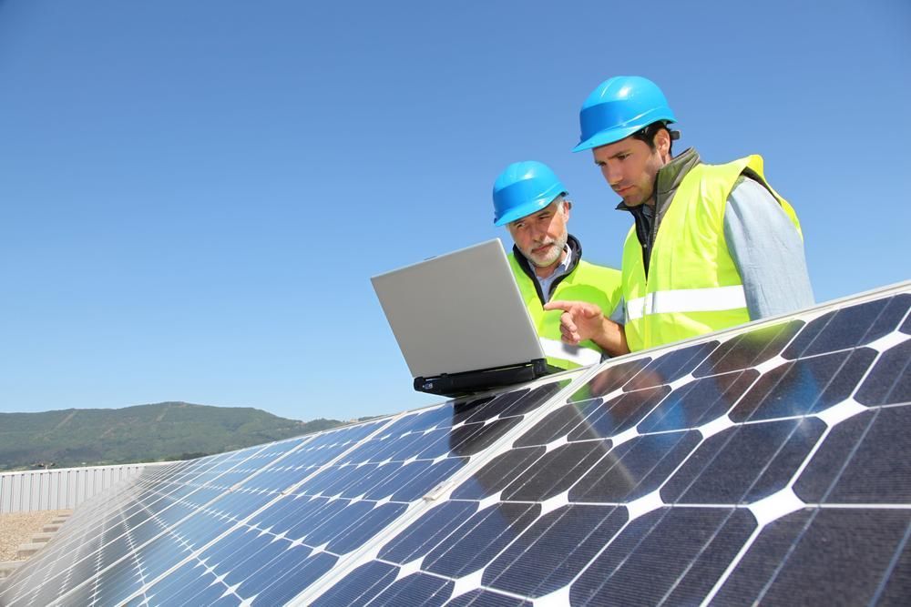 Two Men Are Looking At A Laptop On Top Of A Solar Panel — Mission Solar And Electrical In Tully, QLD