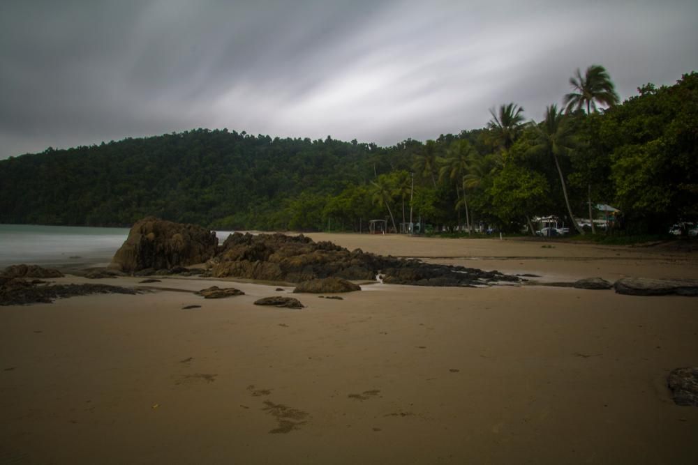 A Beach With Palm Trees And Mountains In The Background On A Cloudy Day — Mission Solar And Electrical In Innisfail, QLD