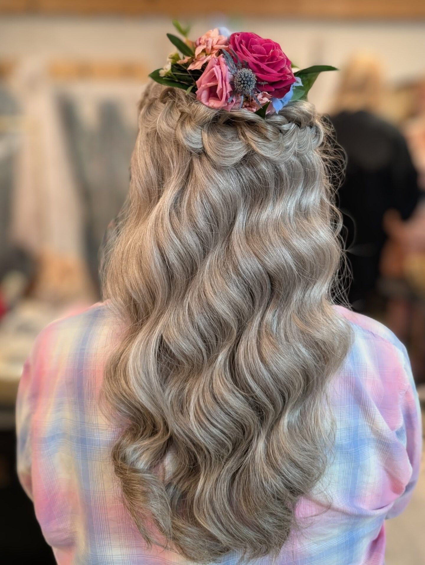 Woman with wavy, light-colored hair, braided at the crown, adorned with flowers.