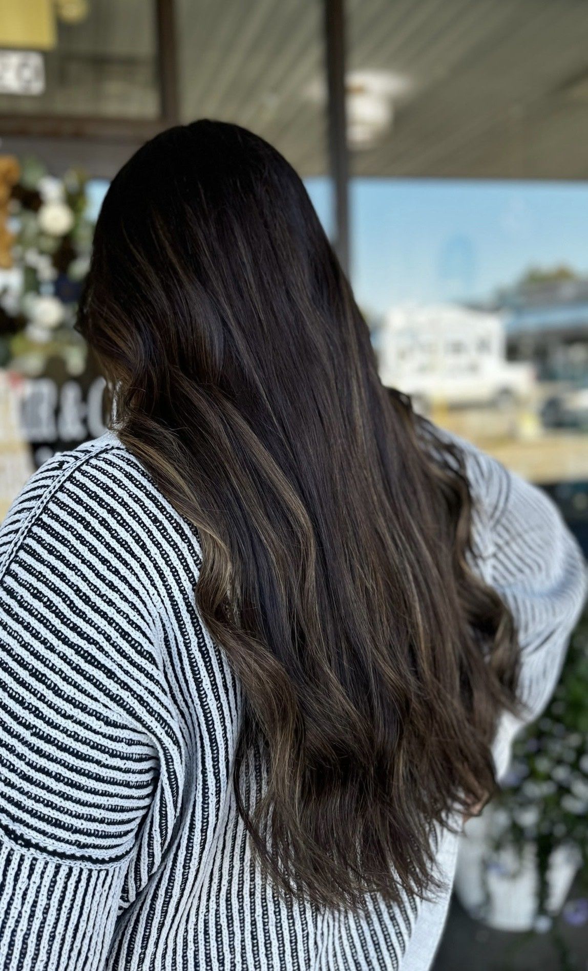 Person with long, dark hair, wearing a striped sweater, standing in front of a window.