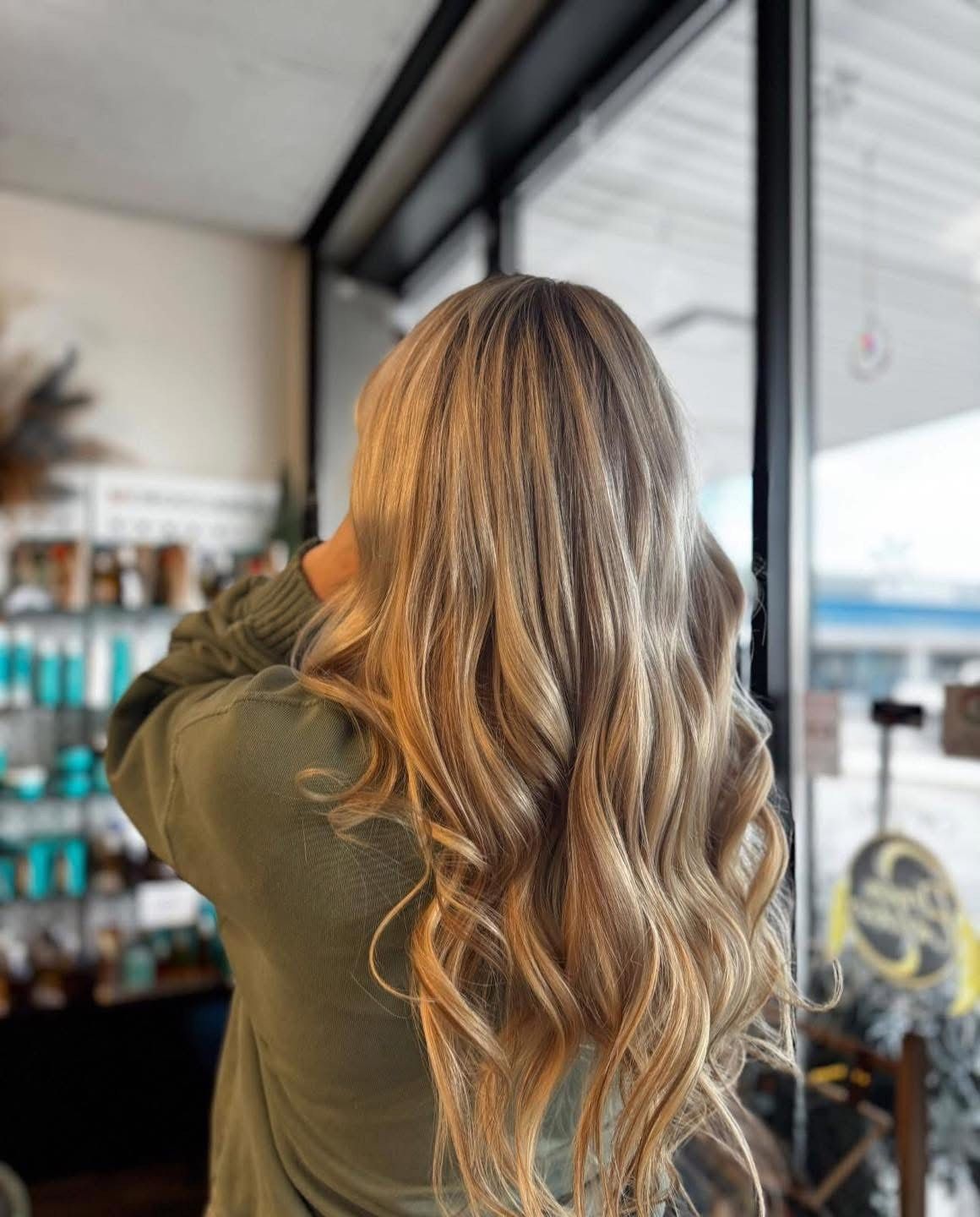 Woman with wavy blonde hair, back to camera, in a salon.