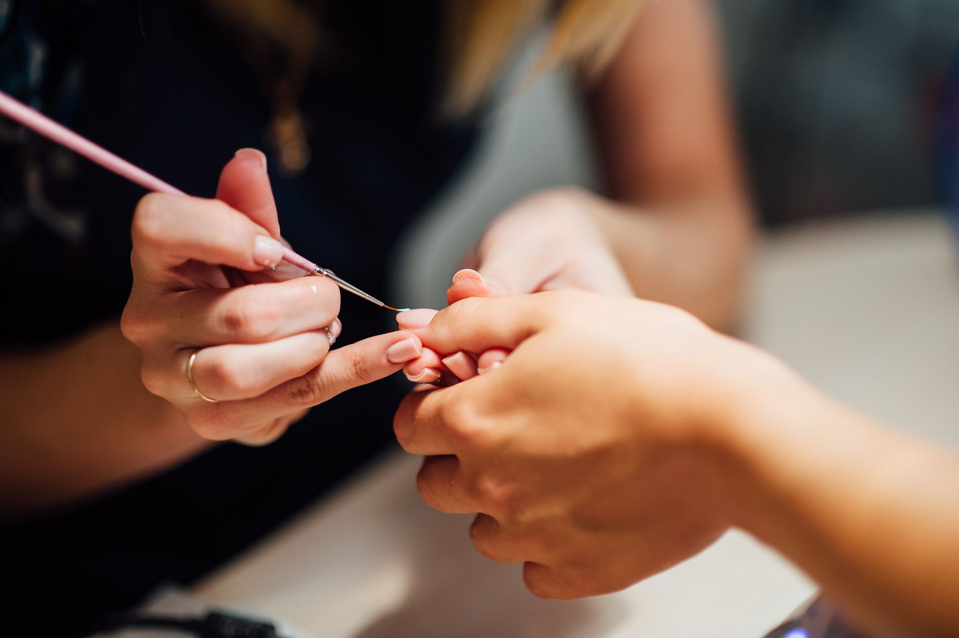 Manicurist applying nail polish to a client's fingernails with a thin brush.