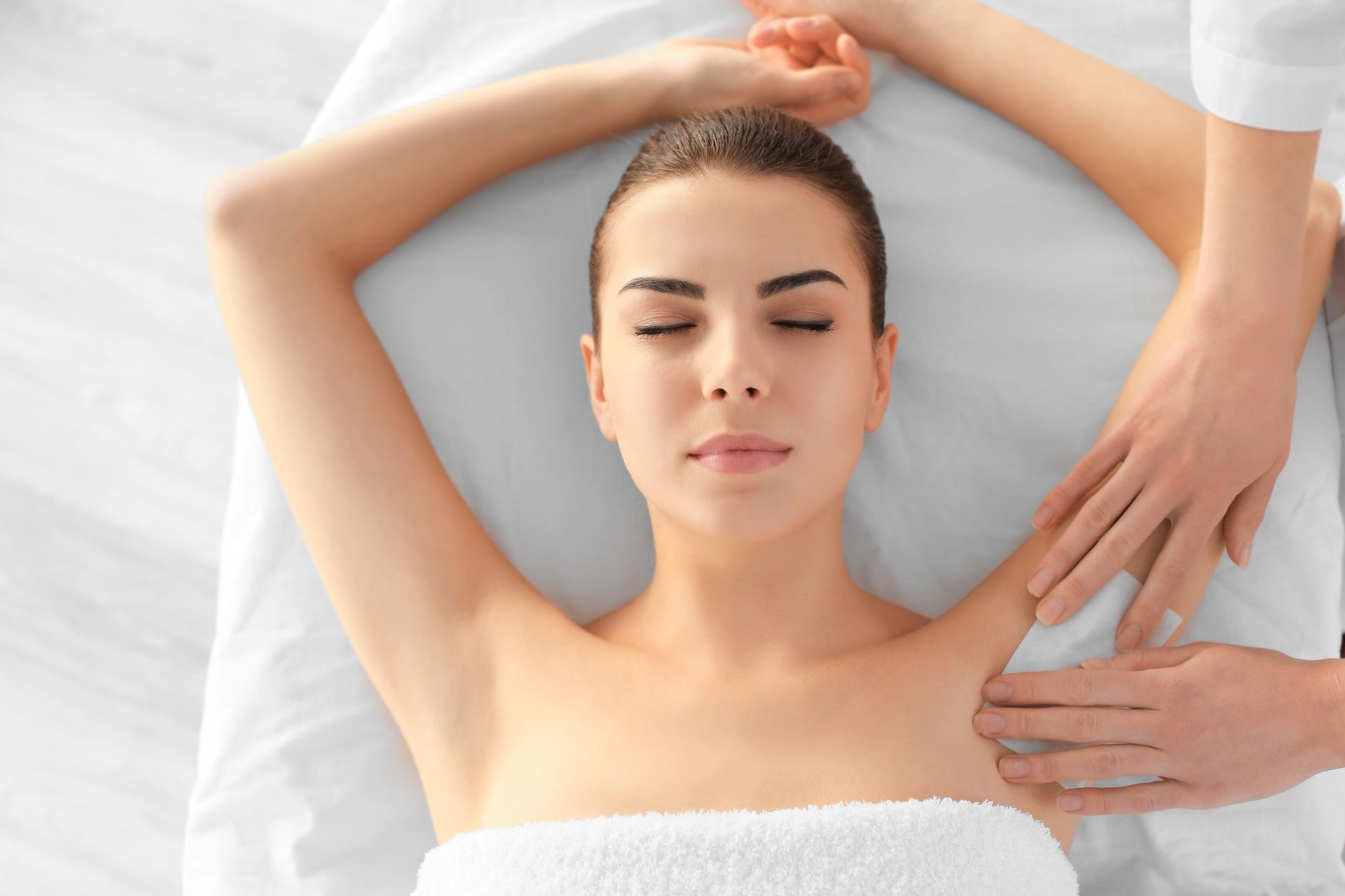 Woman receiving an arm massage at a spa, eyes closed, on a white towel.