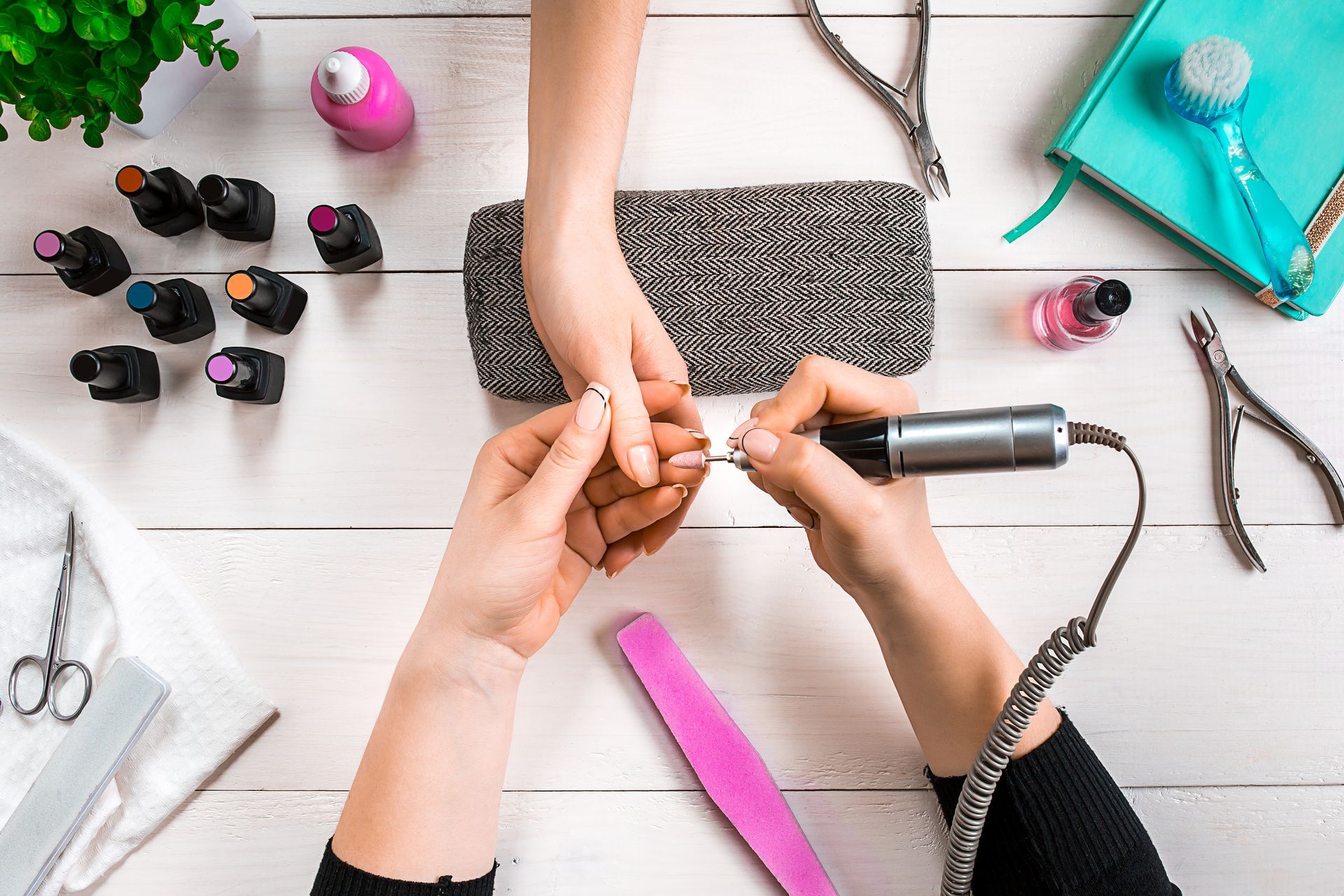 Manicure being performed, using a nail drill and other tools on a white surface.