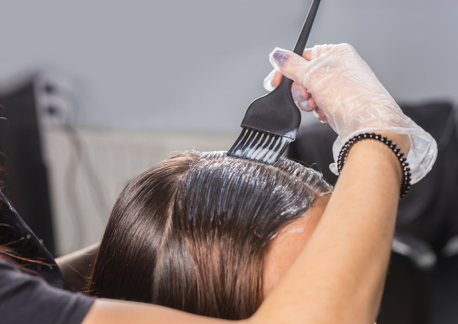 Hairdresser applying dye to a client's hair with a brush, wearing gloves.