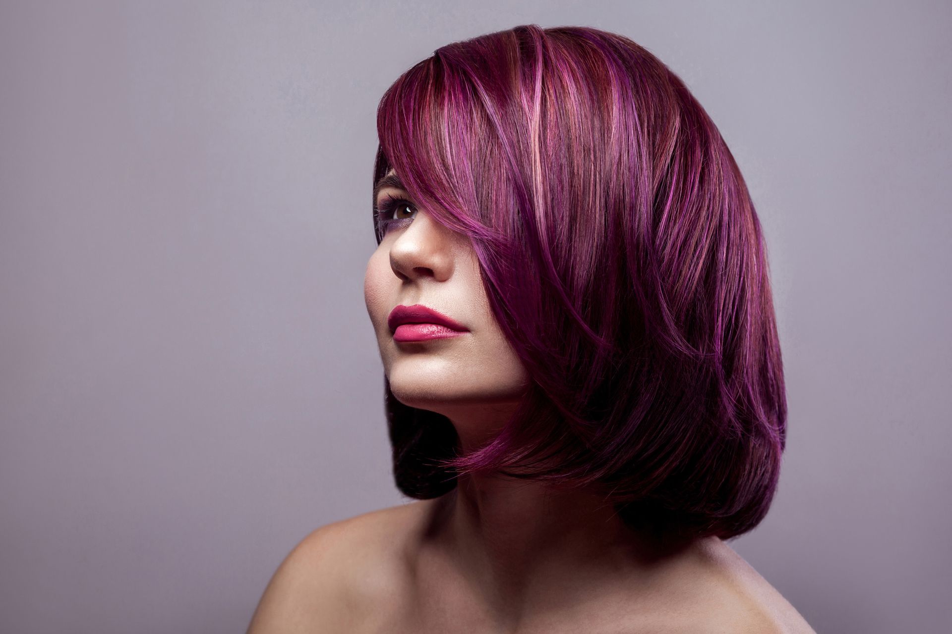 Woman with vibrant purple hair looking upwards, neutral background.