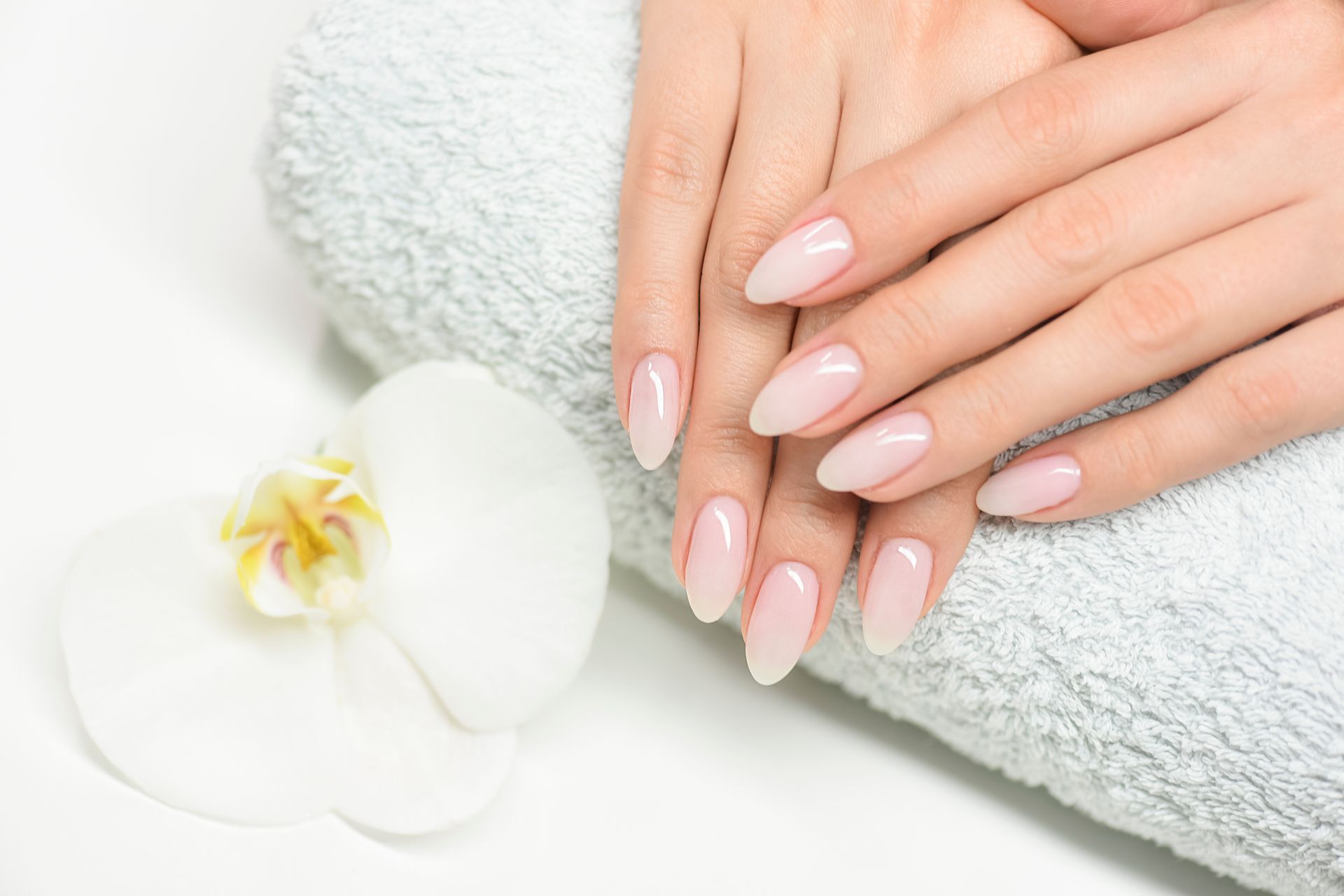 Hands with long, almond-shaped nails. Some are purple glitter, others have delicate floral designs in purple and white.