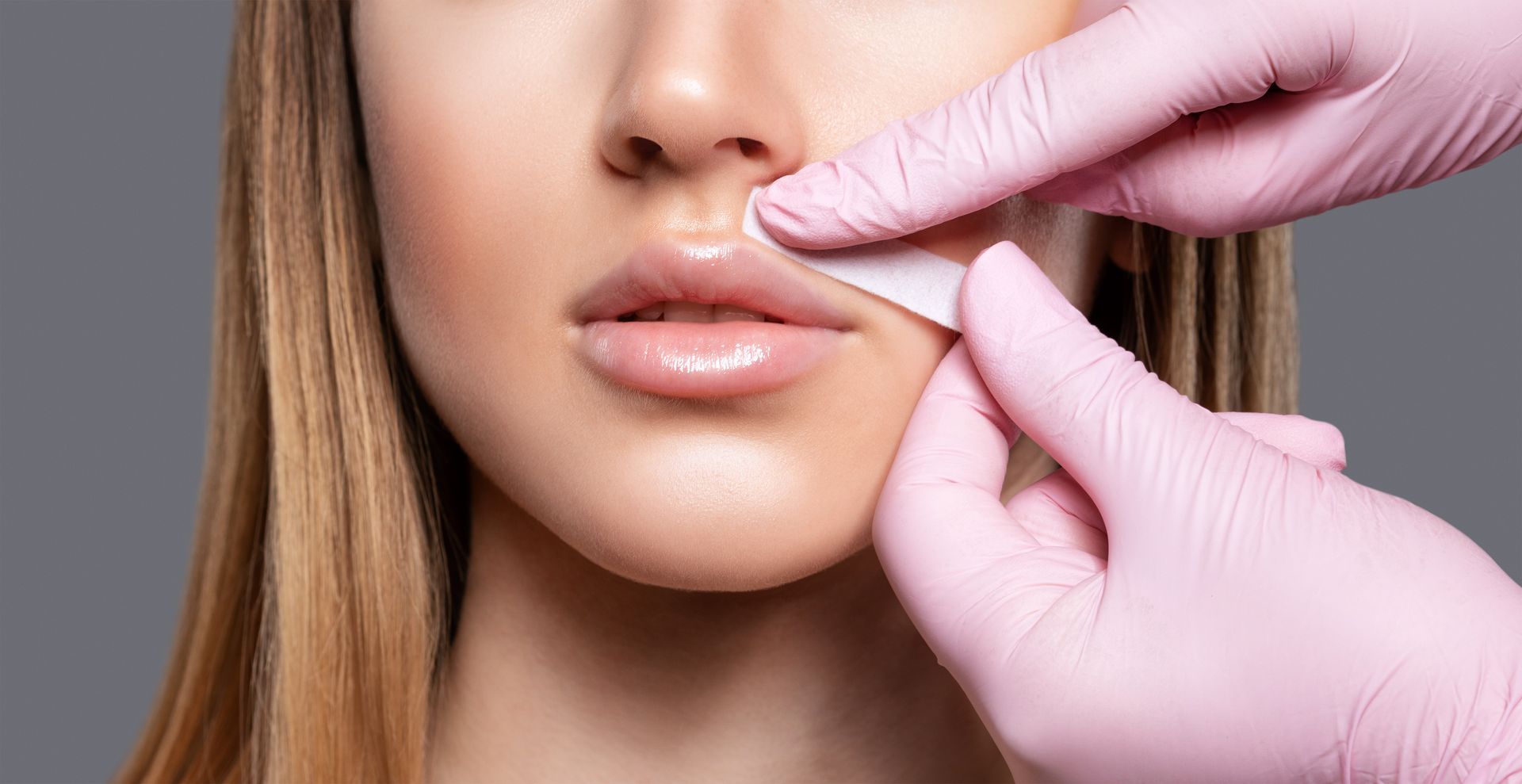 Person's lips being touched with a piece of paper by gloved hands, likely for cosmetic procedure.