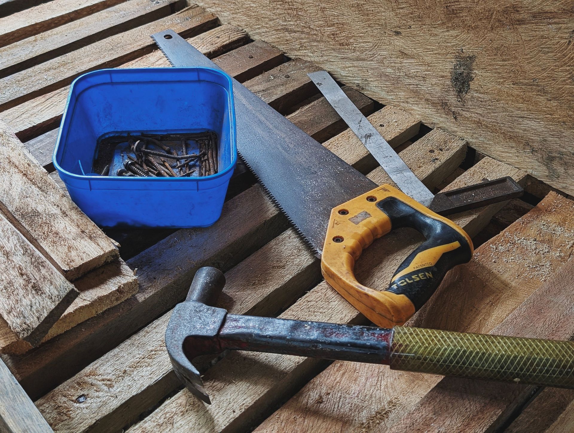 Blue toolbox, handsaw, and hammer on wooden pallets at a worksite