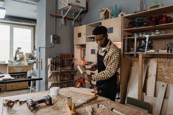Person working in a cluttered woodworking shop, using a hand tool at a workbench.