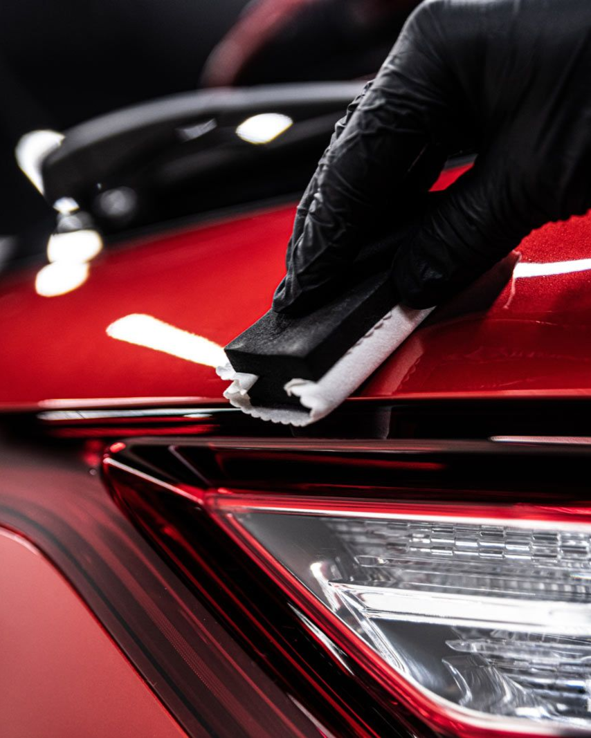 A person wearing black gloves is polishing a black car