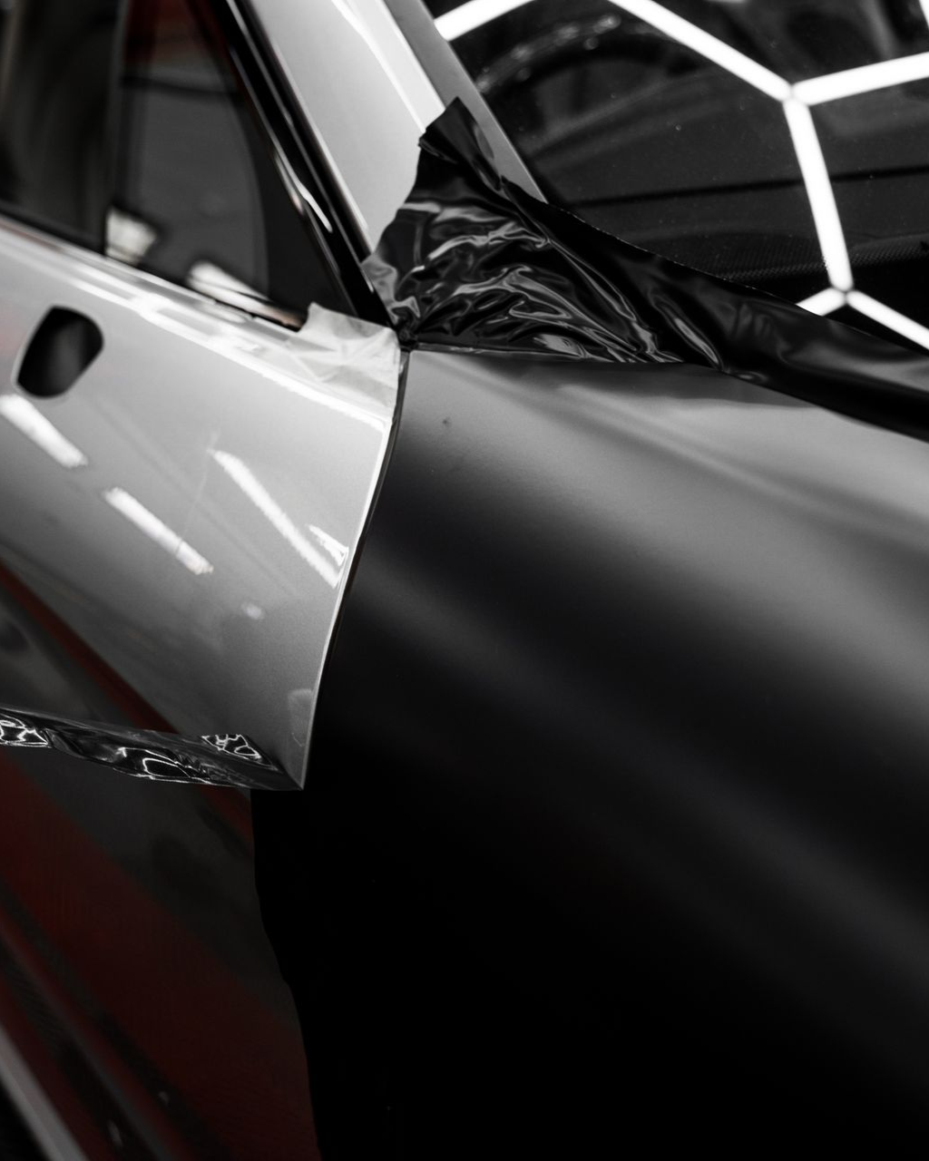 Car panel partially covered with black wrap; white panel adjacent.