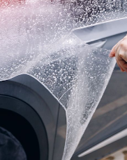 A person is applying a clear film to the hood of a car.