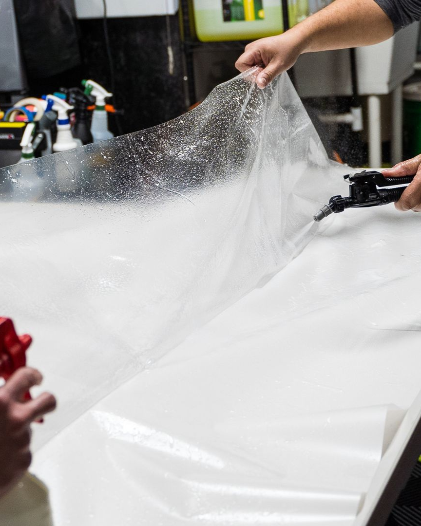 Applying clear protective film to a black car's fender.