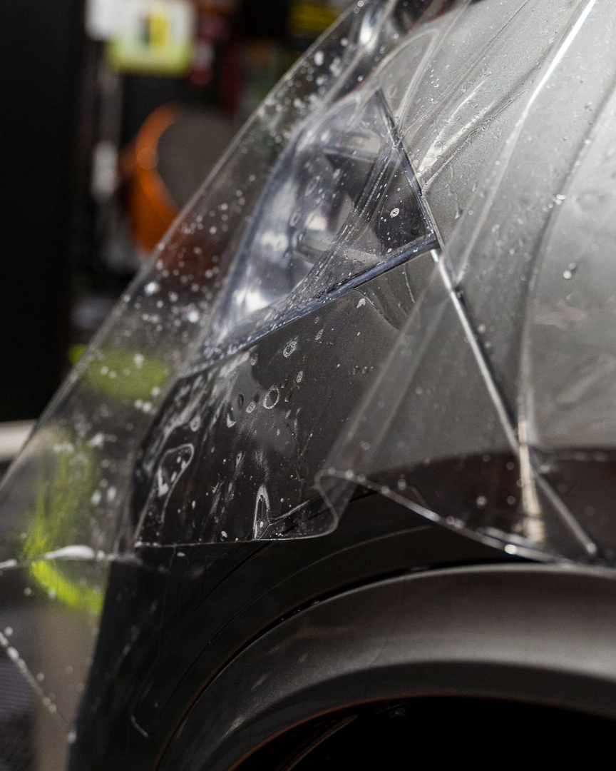 A person is applying a clear film to the hood of a car.