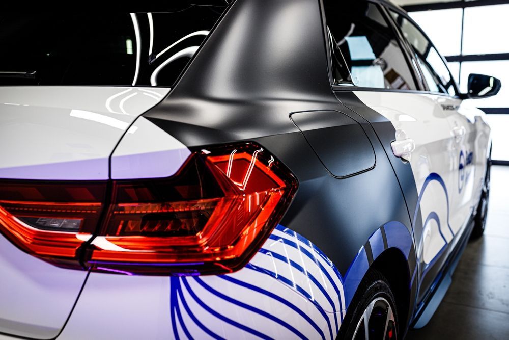 White car with black detailing and blue and white graphics on the rear side panel.