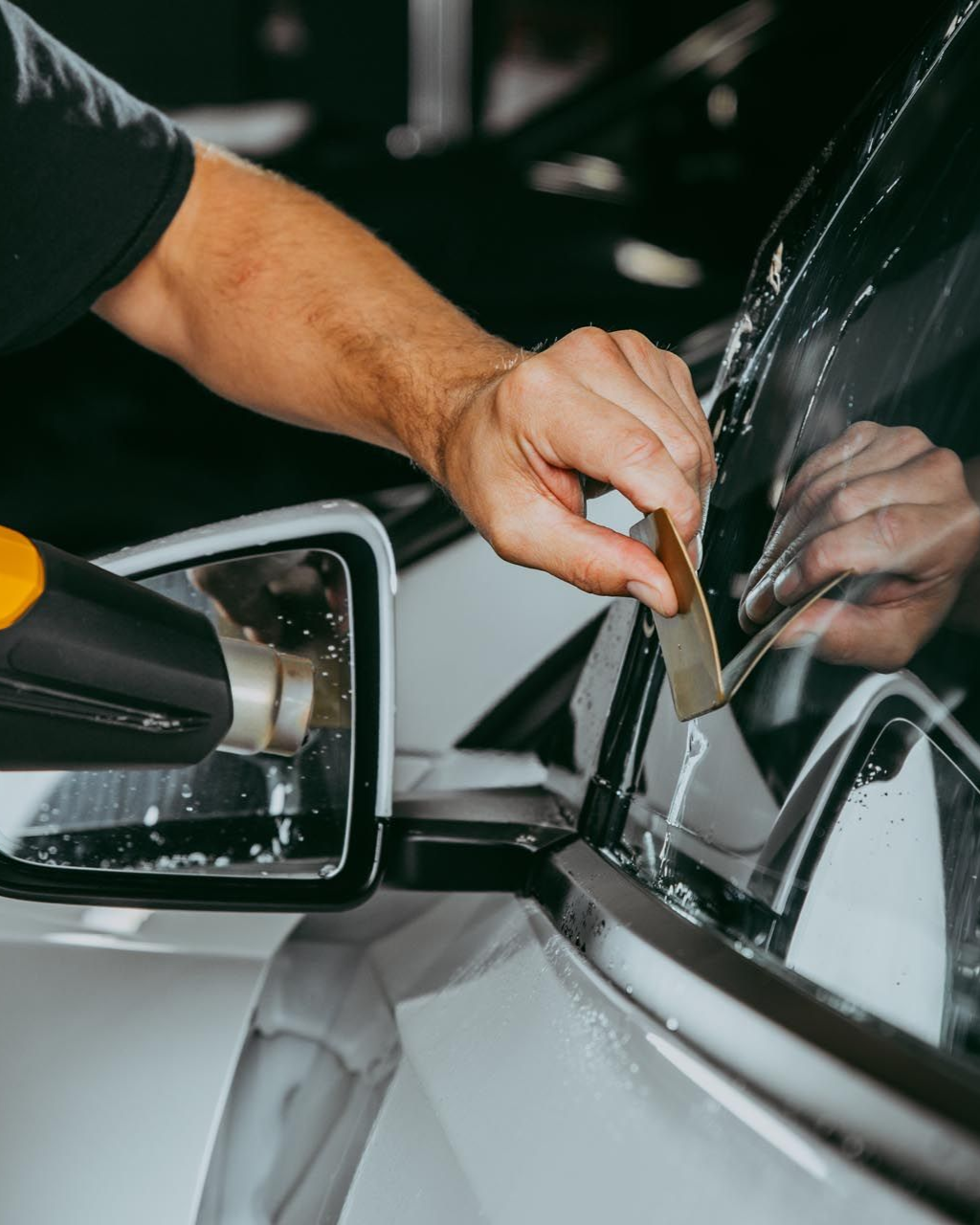 Person applying tint to a car window with a heat gun and squeegee.