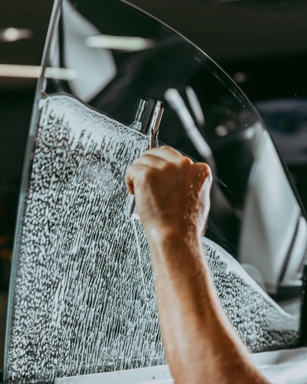 Person applying tint film to a car window with a tool in an indoor setting.